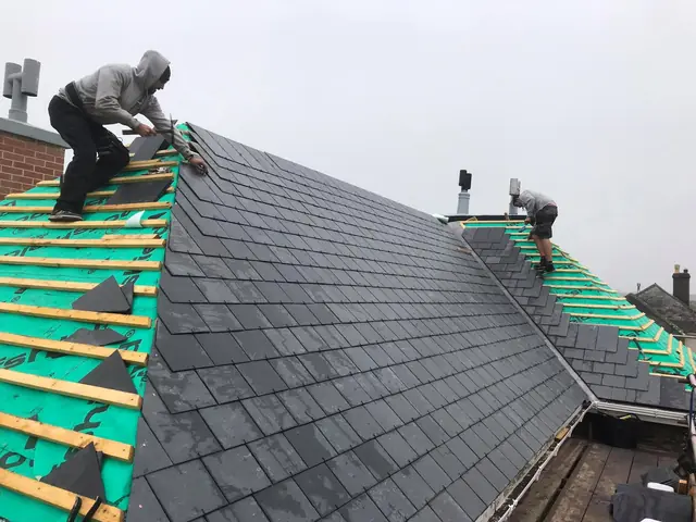 Two roofers slating a hip on a natural slate re-roof