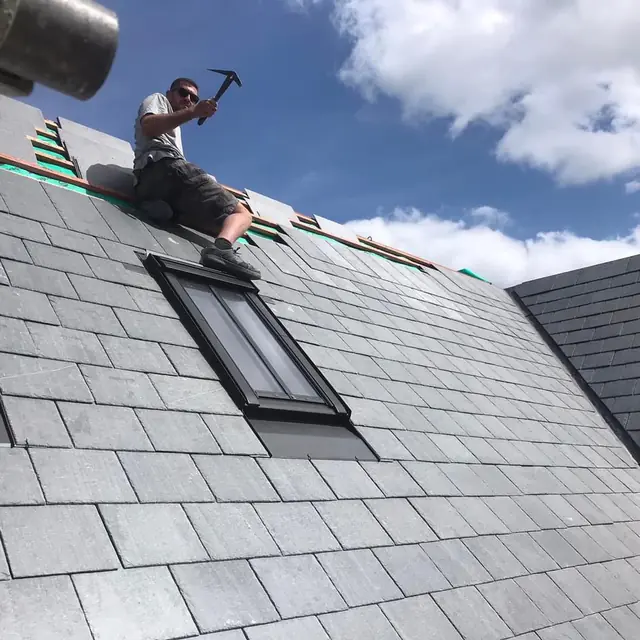 Roofer slating around a new VELUX roof window on a natural slate roof