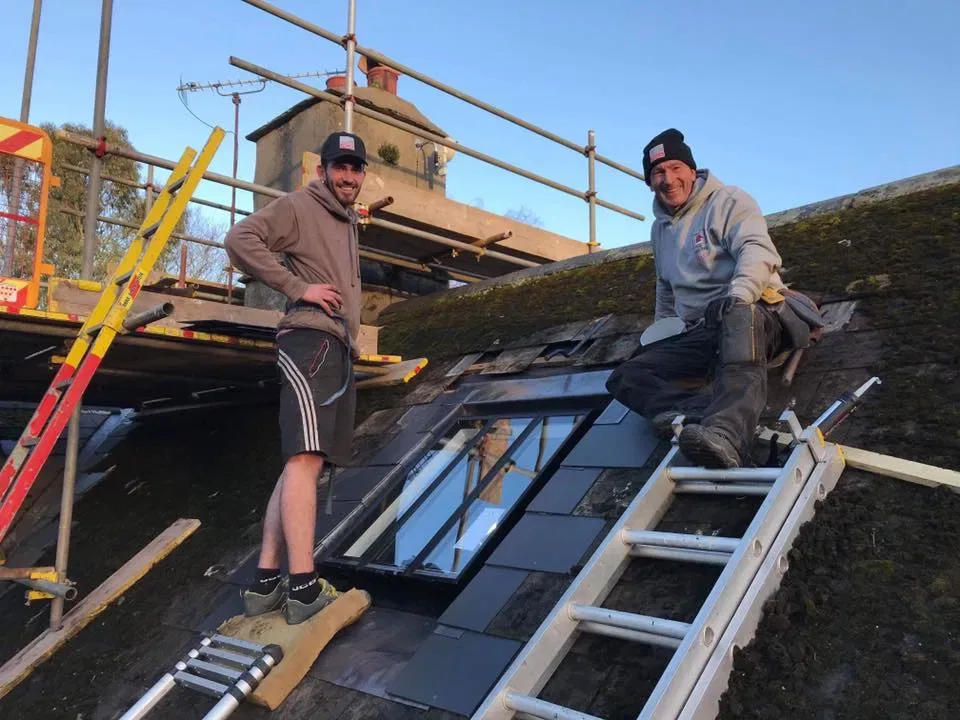 Mark and Sam Dixon on a slate roof beside a newly fitted VELUX roof window